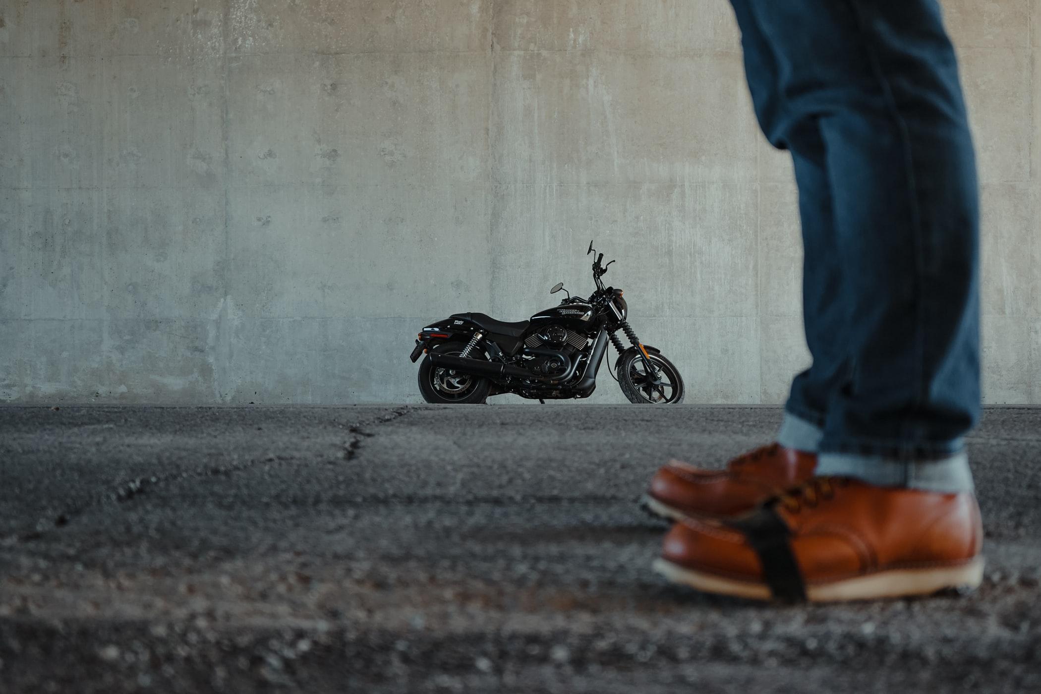 Photo d'une moto noir en fond d'image avec des jambes au devant